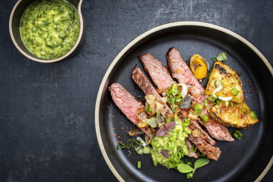 Modern style barbecue dry aged wagyu flank steak with pineapples and chimichurri sauce as top view on a plate