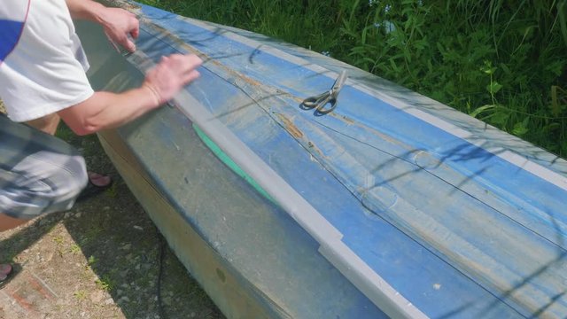 Process of reparing canoe. Man tapes hole on bottom of canoe