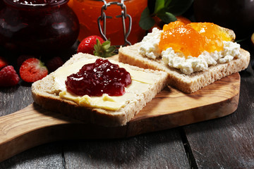 Toast bread with homemade strawberry jam and apricot marmalade on rustic table served with butter for breakfast or brunch