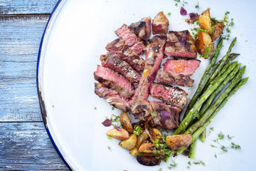 Barbecue dry aged wagyu porterhouse steak sliced with green asparagus and fried potatoes as top view on a plate
