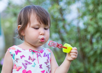 Cute little girl is blowing a soap bubbles.