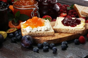 Toast bread with homemade strawberry jam and apricot marmalade on rustic table served with butter for breakfast or brunch