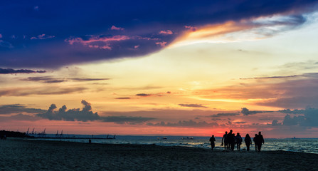 Spacerujący ludzie plażą nad morzem o zachodzie słońca