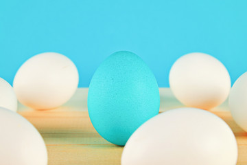 The blue egg won among the white eggs on the wooden table.