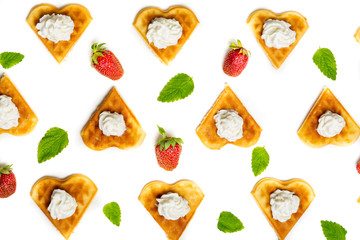 Heart shaped waffles served with cream, strawberries and mint leaves forming an abstract pattern on white background.