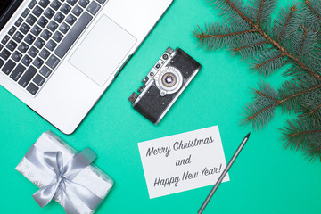 top view of a Christmas tree branch and Christmas, a New Year's gift, a laptop, a retro camera and a greeting card on a green and blue background with space for text. flat lay