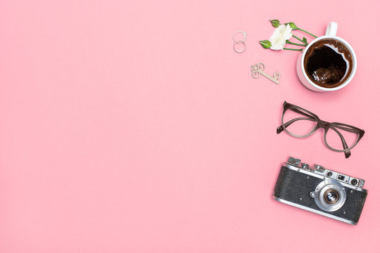 Flay lay, Top view office table desk. Feminine desk workspace frame with cup of coffee, glasses, camera, rings and a rose branch on a pink back ground with space for text