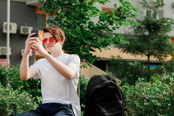 Young man in red glasses take picture on his phone in park