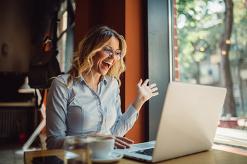 Close shot of smiled blonde woman having online call on laptop while sitting in cafe