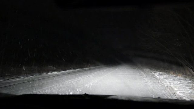 Night driving in the car in the snowfall blizzard on the snow-covered road. Bad weather. Low beam and high beam of headlighs. Road safety