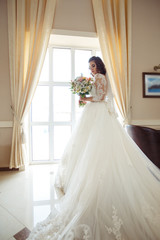 A beautiful bride in a white wedding dress and with a bouquet of flowers enjoying the moment at a beautiful hotel. Great mood, great atmosphere. wedding concept.
