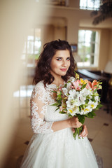 A beautiful bride in a white wedding dress and with a bouquet of flowers enjoying the moment at a beautiful hotel. Great mood, great atmosphere. wedding concept.
