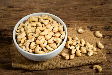 Cashew nuts in white bowl on wooden desk.