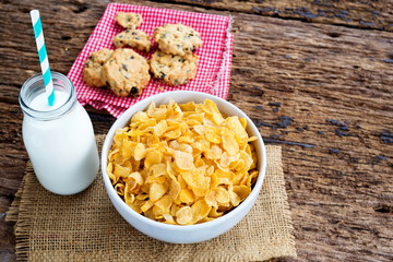 Cornflake cereals on white bowl with milk glass on table.