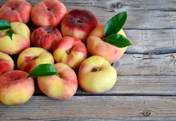 Chinese flat donut peaches with leaves on on old wooden table also known as  Saturn donut, Doughnut peach,
Paraguayo.Healthy eating or diet concept.Selective focus.