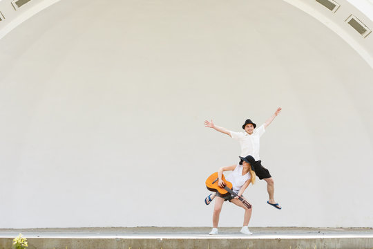 Woman playing guitar, man jumping next to her