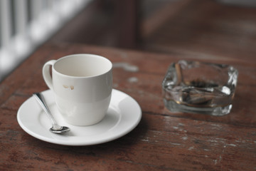 Empty cup of coffee and ashtray on wooden table.