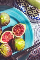 Whole and half cut ripe figs on blue plate; fruit background