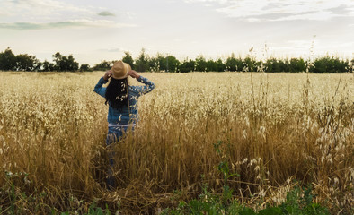 Woman from back with hat in a wheat field, happy woman