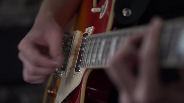 Man quickly strumming power chords on his Les Paul style guitar - close up side shot of his strumming hand