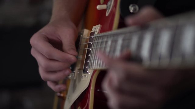 Man goes from picking notes to strumming out chords on a Les Paul styled guitar - close up side shot of his strumming hand