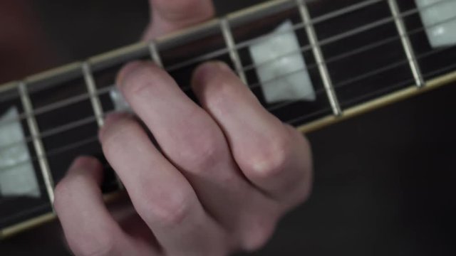 Close up shot of a man's fingers playing rock chords on a Les Paul style guitar