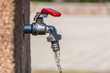 Faucet with red handle and open water outdoor on sunny summer day. Save water concept. Close up, selective focus