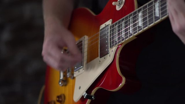 Man starts strumming chords and then starts picks individual strings on a Les Paul style guitar
