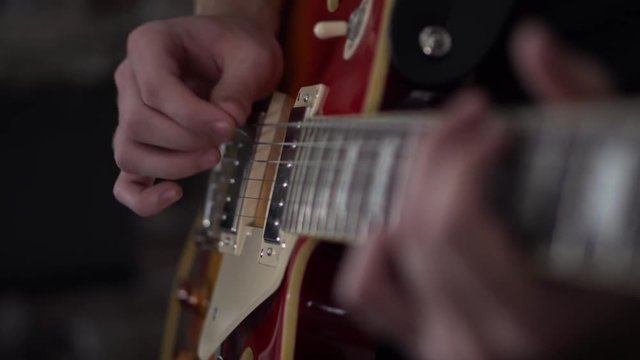 Muted strumming on the low string of a Les Paul style guitar - close up side shot of his strumming hand