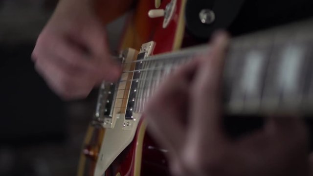 Man strumming on power chords on his Les Paul style guitar - close up side shot of his strumming hand