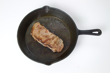 Beef Steak frying in a cast iron skillet isolated on white background