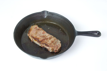 Beef Steak frying in a cast iron skillet isolated on white background