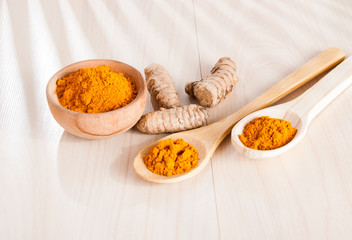Turmeric powder and fresh turmeric on wooden background.