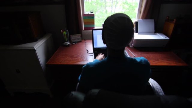 An overhead look at a young Mennonite woman as she types on a laptop computer in slow motion.