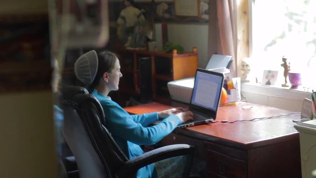 A sliding shot to reveal a young Mennonite woman working on a computer.