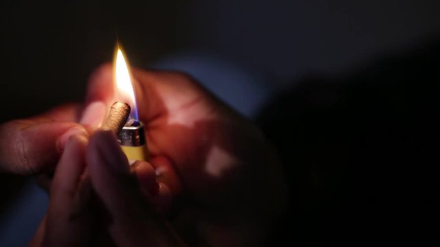 A close up of a hand lighting a blunt and the flame dances in the darkness.