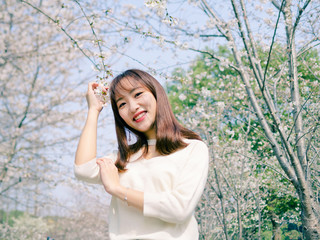 Outdoor portrait of beautiful young Chinese girl smiling among blossom cherry tree brunch in spring garden, beauty, summer, emotion, expression and people concept.