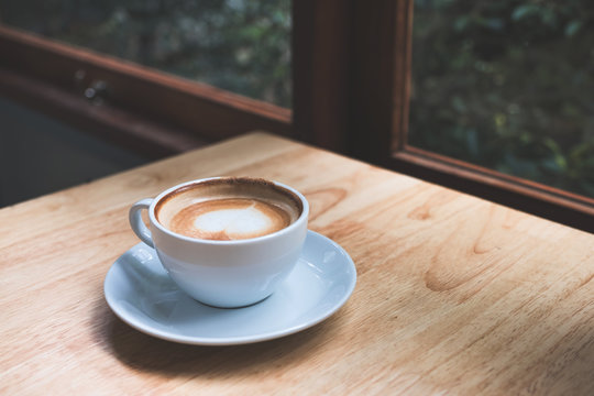Closeup image of hot coffee cup on vintage wooden table in cafe