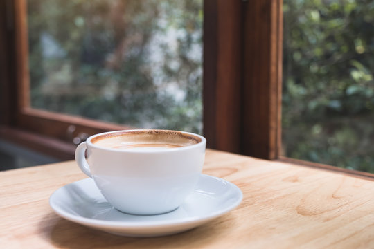 Closeup image of hot coffee cup on vintage wooden table in cafe