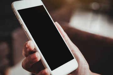 Mockup image of a hand holding white mobile phone with blank black desktop screen with blur background