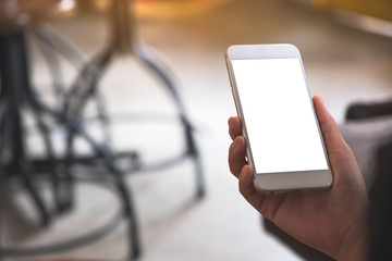 Mockup image of a hand holding white mobile phone with blank desktop screen in cafe