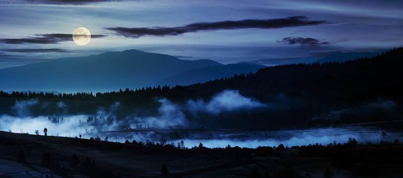panorama of countryside at night in full moon light. beautiful landscape in mountains with fog rising above the valley and hill