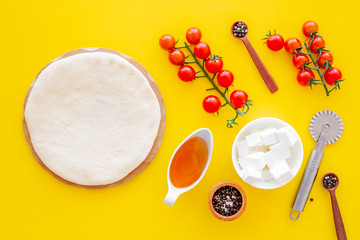 Fototapeta na wymiar Ingredients for cooking pizza. Rolled out pizza dough, cherry tomatoes, olive oil, cheese mozzarella, spices on yellow background top view mockup