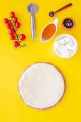 Ingredients for cooking pizza. Rolled out pizza dough, cherry tomatoes, olive oil, cheese mozzarella, spices on yellow background top view mockup