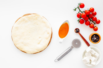 Make pizza concept. Pizza dough and ingredients for filling. Cherry tomatoes, olive oil, cheese mozzarella, spices near knife for pizza on white background top view mockup
