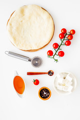 Make pizza concept. Pizza dough and ingredients for filling. Cherry tomatoes, olive oil, cheese mozzarella, spices near knife for pizza on white background top view mockup