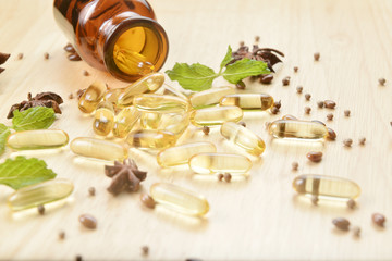 Fish oil capsules with omega 3 and vitamin D spread out of a  brown glass bottle on wooden texture, healthy diet concept.