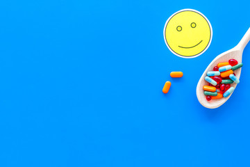 Reception of medicines concept. Recovery. Pills in spoon near smile face emoji on blue background top view space for text