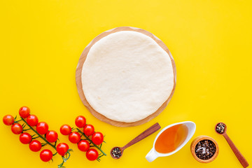 Ingredients for cooking vegetarian pizza. Rolled pizza dough, cherry tomatoes, olive oil, cheese mozzarella, spices on yellow background top view mockup copy space