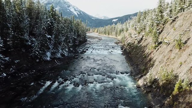 Aerial shot over river with rising pan towards mountains in Banff